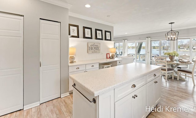 kitchen with an inviting chandelier, light wood-style floors, ornamental molding, white cabinetry, and a center island