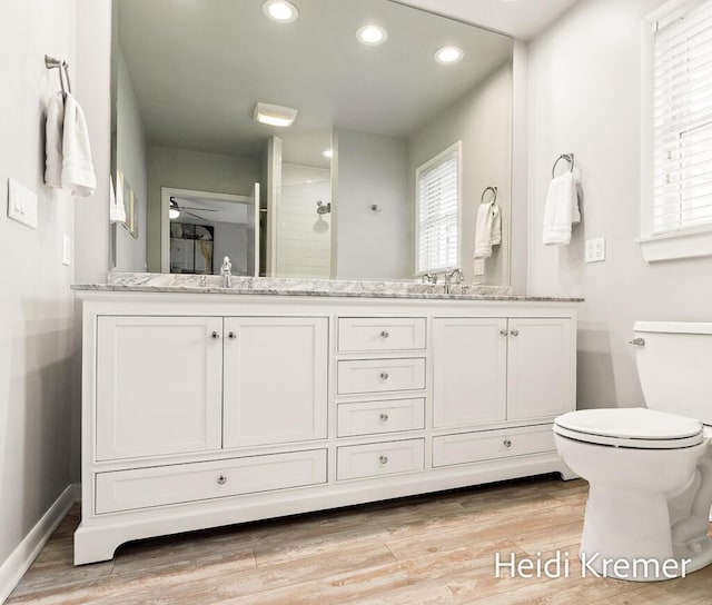 bathroom with recessed lighting, wood finished floors, double vanity, toilet, and a sink