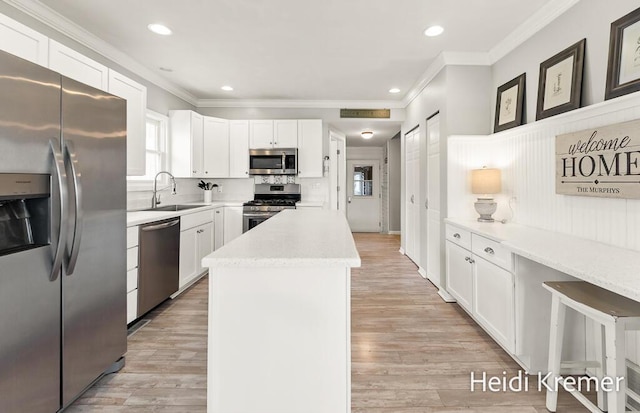 kitchen featuring crown molding, a sink, appliances with stainless steel finishes, and a kitchen island
