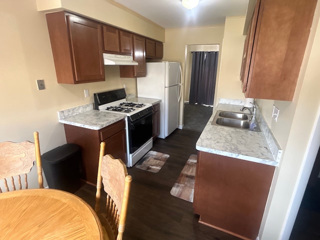 kitchen with light countertops, under cabinet range hood, range with gas cooktop, a sink, and dark wood finished floors