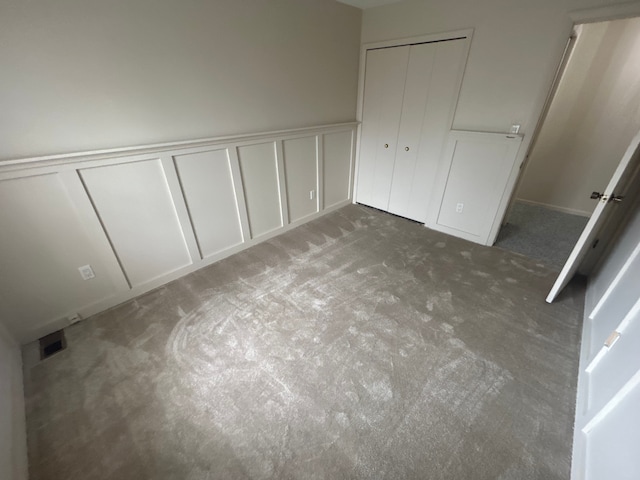 unfurnished bedroom with a wainscoted wall, carpet, a decorative wall, and visible vents