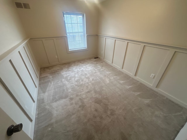 interior space featuring a wainscoted wall, light carpet, a decorative wall, and visible vents
