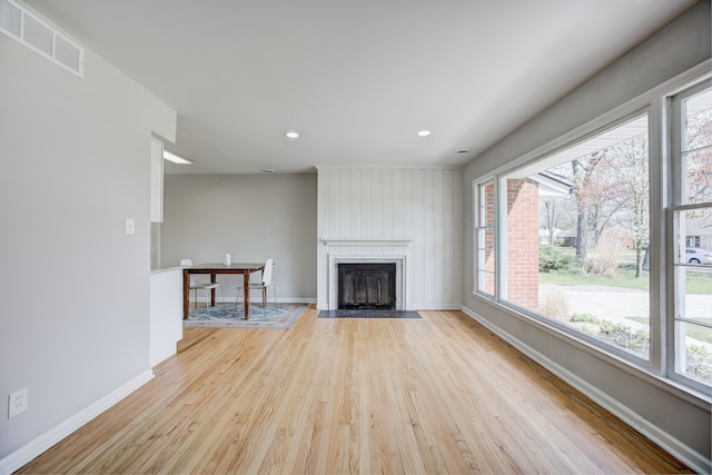 unfurnished living room with a large fireplace, baseboards, light wood finished floors, and visible vents