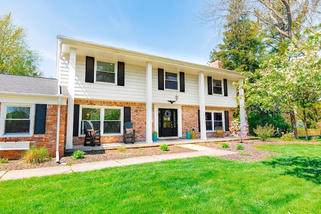 view of front of home with a porch, brick siding, a front yard, and a chimney