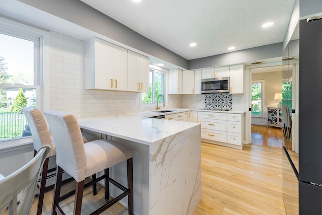 kitchen with white cabinets, a sink, a breakfast bar area, a peninsula, and stainless steel microwave