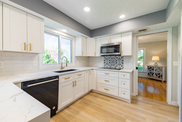kitchen featuring a sink, white cabinets, stainless steel microwave, light wood finished floors, and black dishwasher