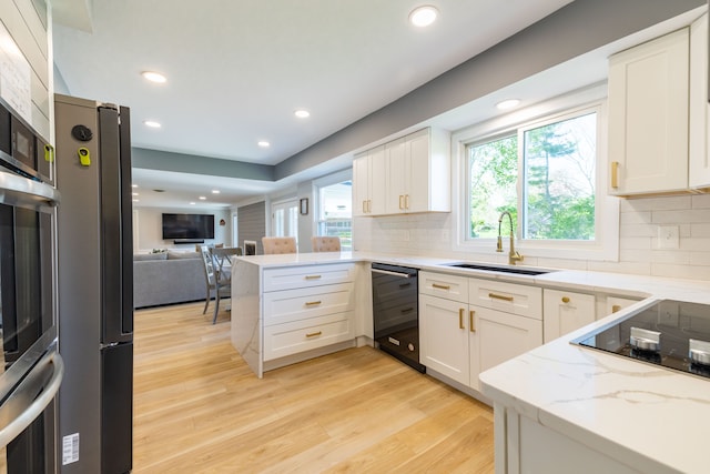kitchen with a sink, a peninsula, open floor plan, tasteful backsplash, and black appliances