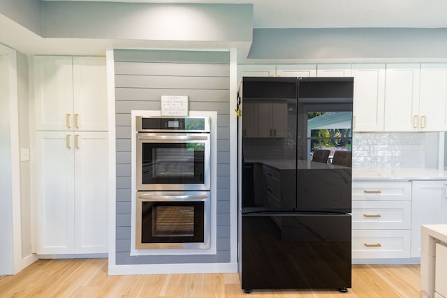 kitchen featuring stainless steel double oven, light wood finished floors, white cabinets, and black refrigerator