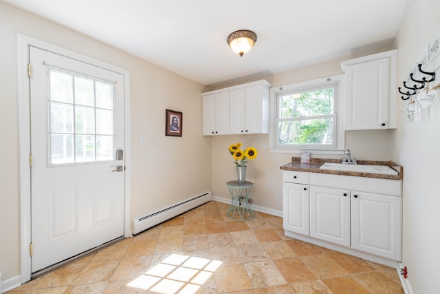 clothes washing area featuring stone finish floor, baseboards, a sink, and baseboard heating