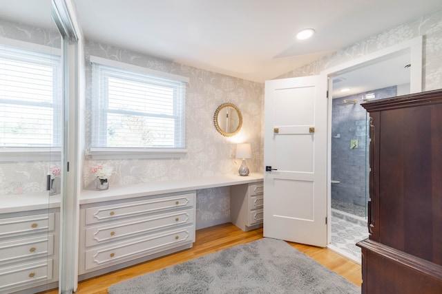 office space with light wood finished floors, built in desk, and wallpapered walls