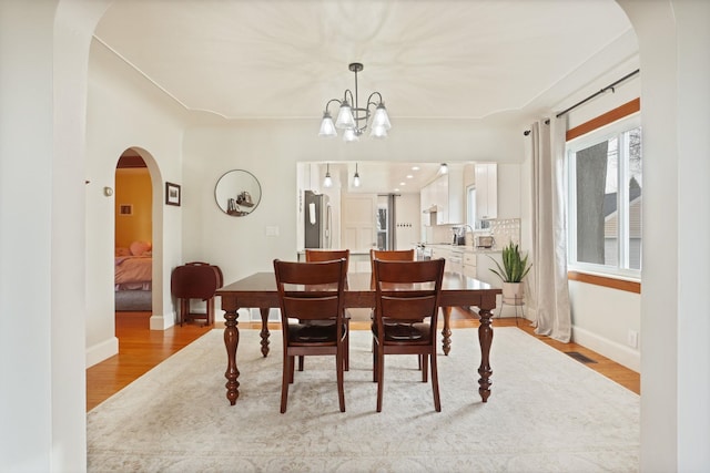 1743 Midland Rd, Bay City, MI 48706 - dining area featuring arched walkways, light wood-style floors, a chandelier, and baseboards