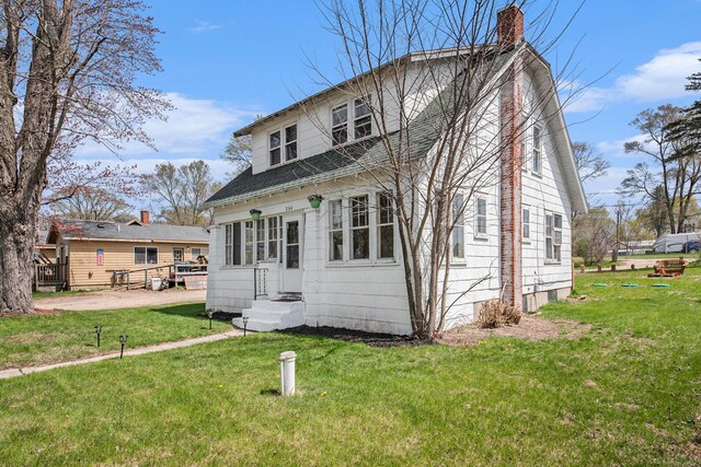 view of front of property with roof with shingles, a front yard, and a chimney