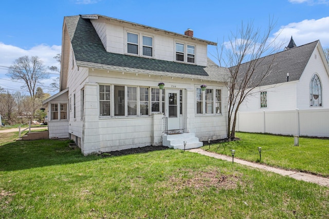 view of front of home with a chimney, roof with shingles, fence, a front lawn, and entry steps