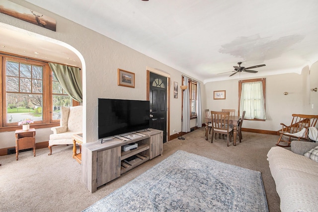 living area featuring a ceiling fan, baseboards, and light carpet