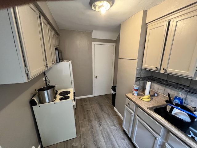 kitchen with a sink, tasteful backsplash, light countertops, freestanding refrigerator, and dark wood finished floors