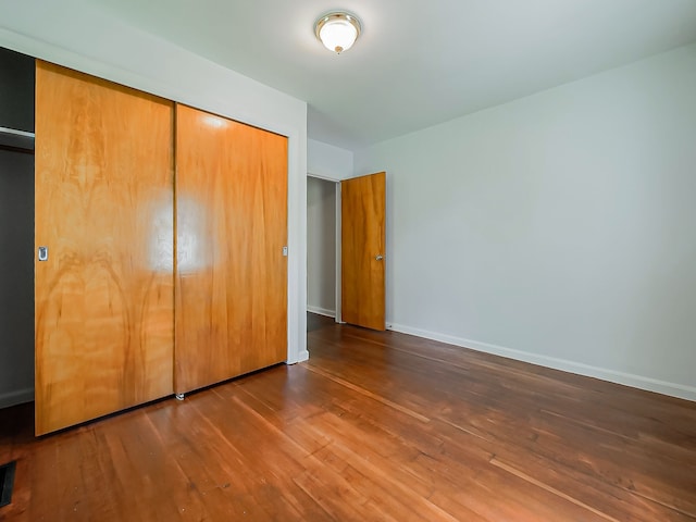 unfurnished bedroom featuring wood-type flooring, a closet, and baseboards