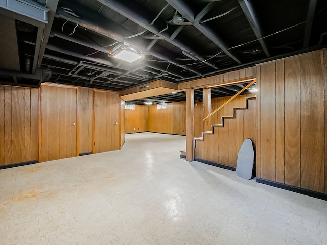 finished below grade area with light floors, wood walls, and stairway