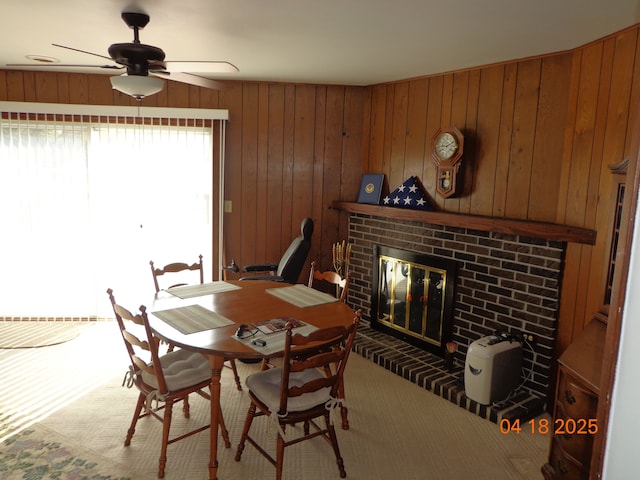 carpeted dining room with wooden walls, ceiling fan, and a brick fireplace