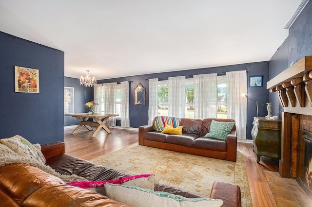 living room with a brick fireplace, wood finished floors, a chandelier, and baseboards