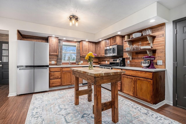 kitchen featuring wood finished floors, stainless steel appliances, open shelves, light countertops, and a sink