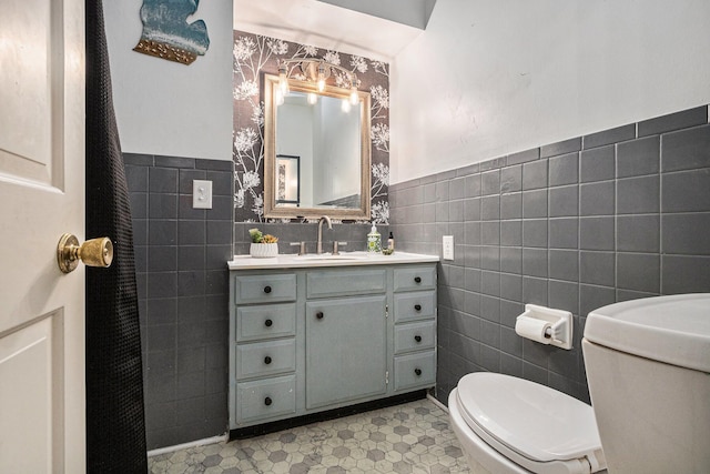 bathroom featuring vanity, toilet, wainscoting, and tile walls
