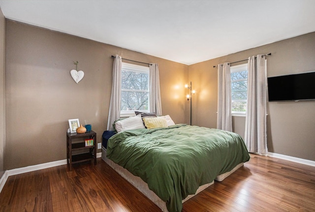 bedroom with multiple windows, wood finished floors, and baseboards