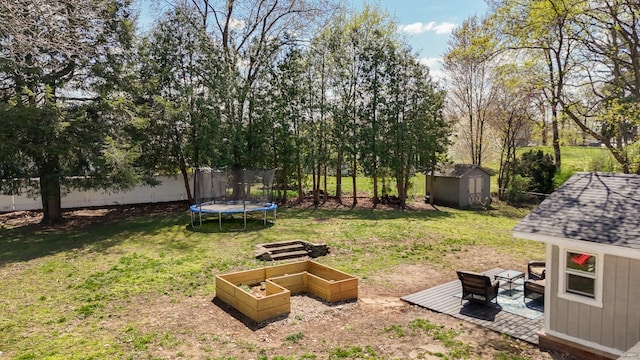 view of yard with a trampoline, an outdoor structure, fence, a shed, and a vegetable garden