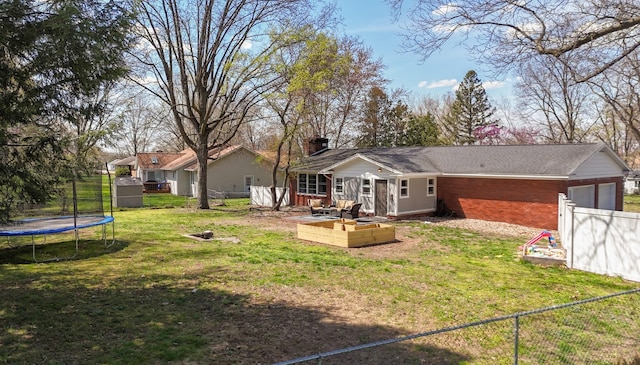 rear view of property with an attached garage, a trampoline, a fire pit, and fence