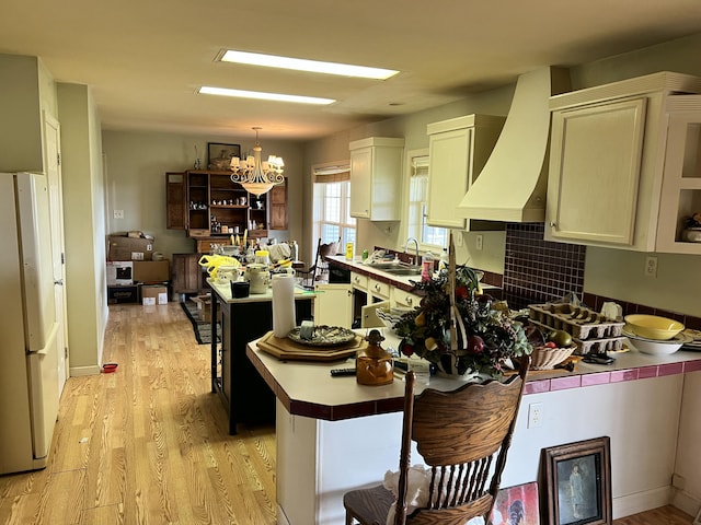 kitchen featuring a sink, light wood-style floors, freestanding refrigerator, an inviting chandelier, and custom exhaust hood