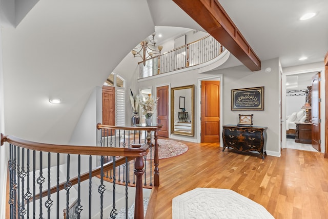 corridor with an upstairs landing, light wood-style floors, baseboards, recessed lighting, and a towering ceiling