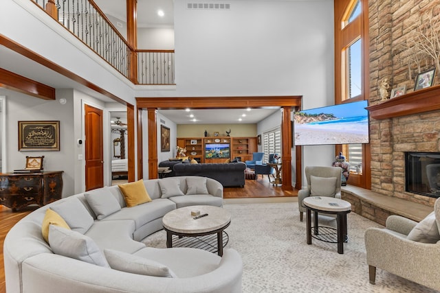 living area with visible vents, wood finished floors, a high ceiling, and a stone fireplace