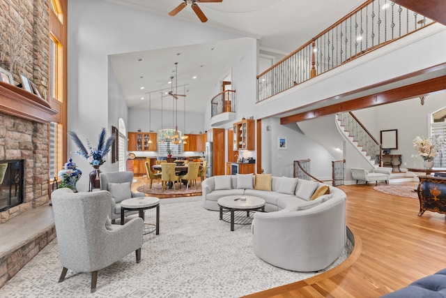 living room with a fireplace, high vaulted ceiling, ceiling fan, stairs, and wood finished floors