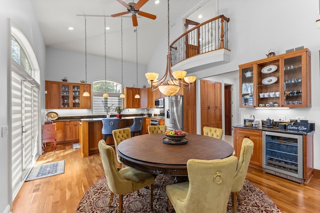 dining room featuring beverage cooler, light wood finished floors, high vaulted ceiling, and a ceiling fan