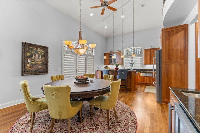 dining space featuring a ceiling fan, high vaulted ceiling, light wood-style flooring, and baseboards