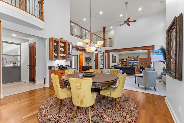 dining room with a towering ceiling, baseboards, light wood-style flooring, and ceiling fan with notable chandelier