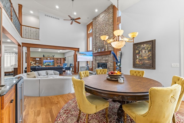 dining space featuring ceiling fan, visible vents, a stone fireplace, light wood-style flooring, and a towering ceiling