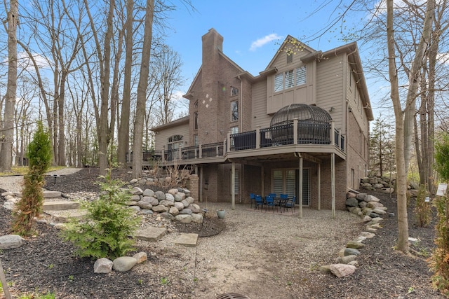 back of house featuring brick siding, a wooden deck, a patio area, and a chimney