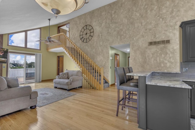 9015 Kingsley Dr, Onsted, MI 49265 - living room with visible vents, light wood-style floors, a towering ceiling, a ceiling fan, and stairs