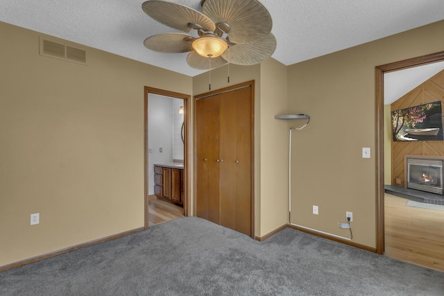 9015 Kingsley Dr, Onsted, MI 49265 - unfurnished bedroom featuring a warm lit fireplace, visible vents, baseboards, a textured ceiling, and light colored carpet