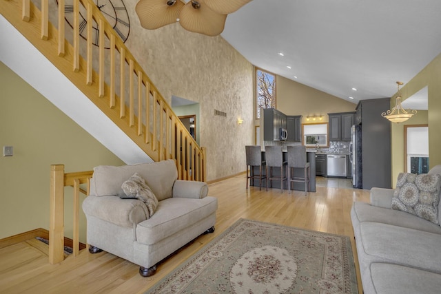 9015 Kingsley Dr, Onsted, MI 49265 - living area featuring baseboards, high vaulted ceiling, stairs, and light wood finished floors