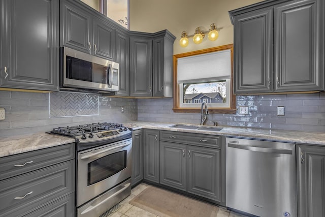 9015 Kingsley Dr, Onsted, MI 49265 - kitchen featuring a sink, decorative backsplash, light stone counters, gray cabinetry, and appliances with stainless steel finishes