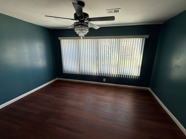 empty room featuring a ceiling fan, visible vents, wood finished floors, and baseboards
