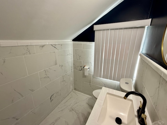 bathroom with lofted ceiling, a sink, toilet, tile walls, and marble finish floor