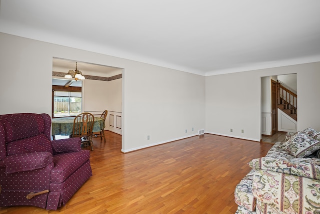 living area featuring an inviting chandelier, ornamental molding, wood finished floors, stairway, and a wainscoted wall