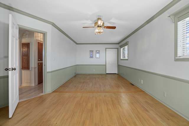 spare room with a ceiling fan, visible vents, ornamental molding, and light wood finished floors