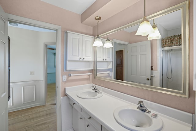 bathroom featuring a sink, a wainscoted wall, double vanity, and wood finished floors