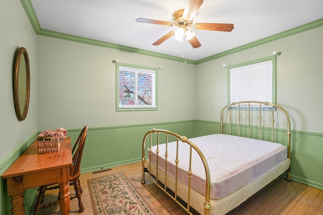 bedroom with crown molding, visible vents, baseboards, ceiling fan, and hardwood / wood-style flooring