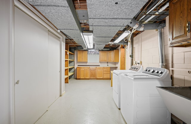 clothes washing area with a sink, concrete block wall, cabinet space, and washer and dryer