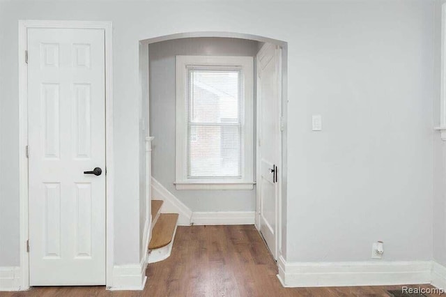 corridor featuring arched walkways, wood finished floors, and baseboards