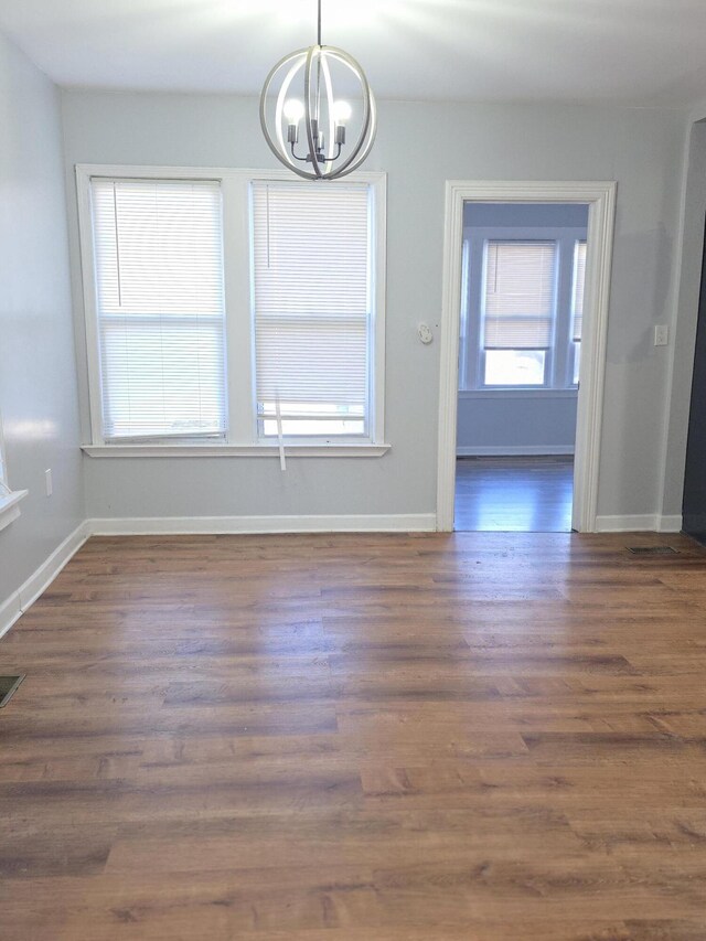 unfurnished dining area featuring dark wood-style flooring, visible vents, a notable chandelier, and baseboards